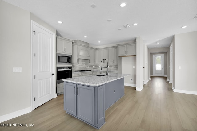 kitchen with gray cabinetry, sink, black appliances, light hardwood / wood-style floors, and an island with sink