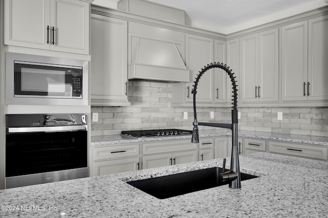 kitchen with decorative backsplash, light stone counters, custom range hood, and appliances with stainless steel finishes