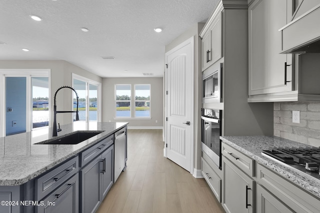 kitchen with decorative backsplash, appliances with stainless steel finishes, sink, light hardwood / wood-style flooring, and an island with sink