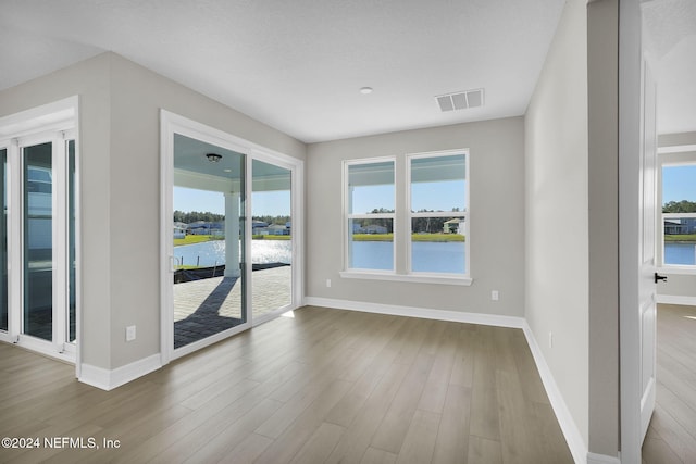 empty room featuring hardwood / wood-style flooring, a water view, and a textured ceiling