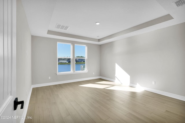 spare room with a raised ceiling, light hardwood / wood-style flooring, and a water view