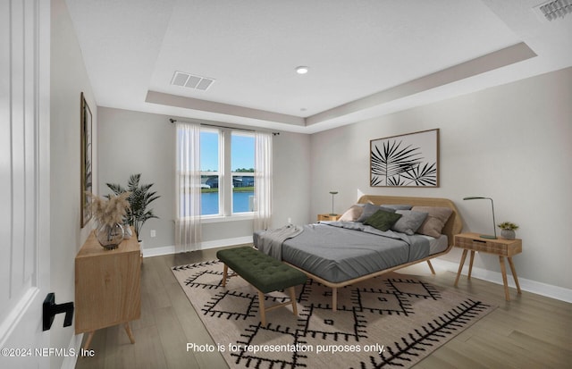 bedroom with wood-type flooring, a water view, and a raised ceiling