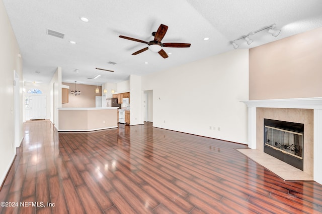 unfurnished living room with ceiling fan with notable chandelier, a textured ceiling, rail lighting, and dark wood-type flooring