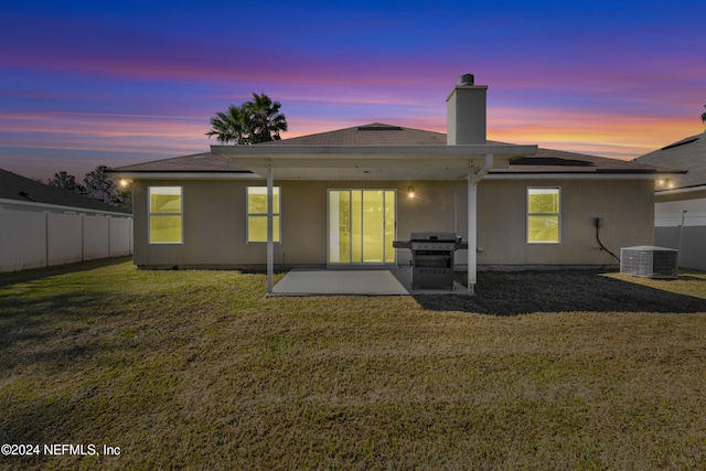 back house at dusk with a yard, a patio, and central AC unit