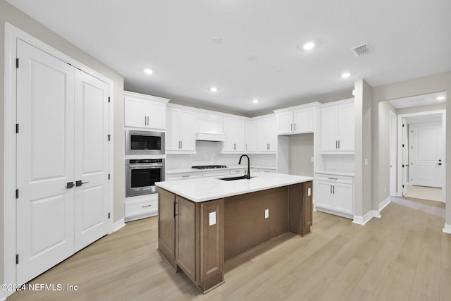 kitchen featuring a center island with sink, white cabinets, stainless steel appliances, and light hardwood / wood-style flooring