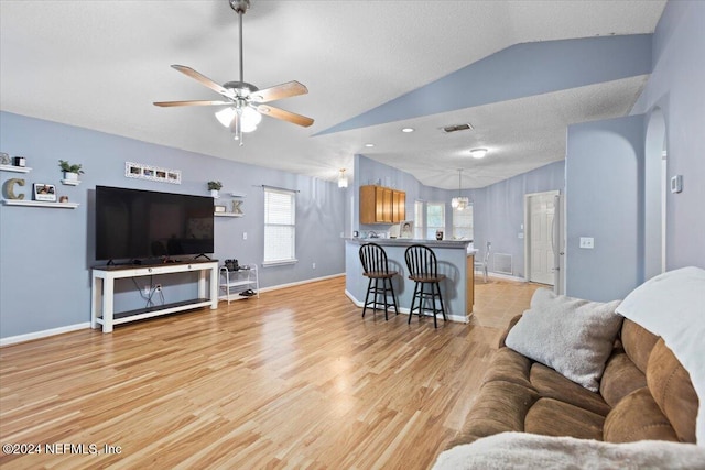 living room with a textured ceiling, light hardwood / wood-style flooring, ceiling fan with notable chandelier, and vaulted ceiling