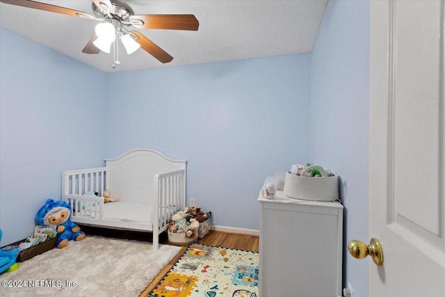 bedroom with a crib, wood-type flooring, a textured ceiling, and ceiling fan