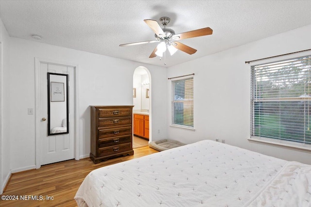 bedroom featuring ceiling fan, a textured ceiling, connected bathroom, and light hardwood / wood-style flooring