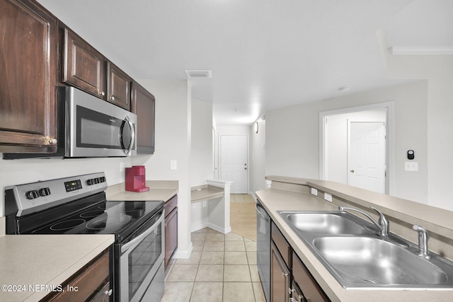 kitchen with dark brown cabinetry, sink, light tile patterned floors, and stainless steel appliances