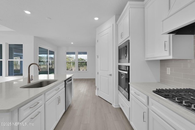 kitchen with a sink, decorative backsplash, custom range hood, white cabinets, and appliances with stainless steel finishes