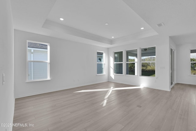 empty room with a tray ceiling, light wood-style flooring, visible vents, and a wealth of natural light