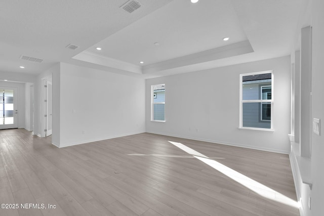 empty room featuring visible vents, light wood-style flooring, and a raised ceiling