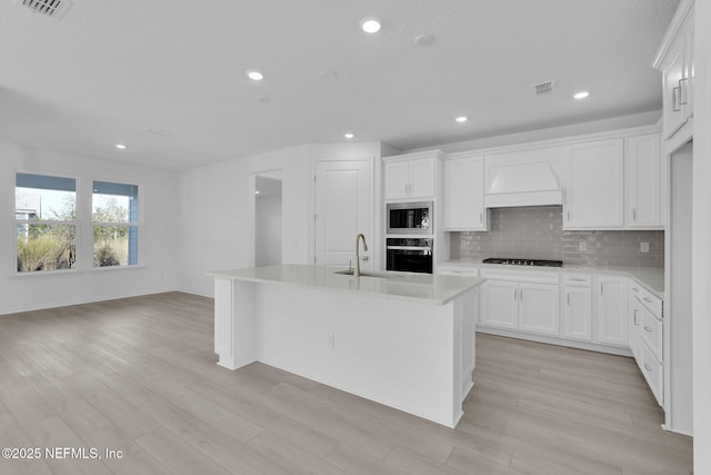 kitchen featuring tasteful backsplash, stainless steel microwave, oven, custom exhaust hood, and a sink