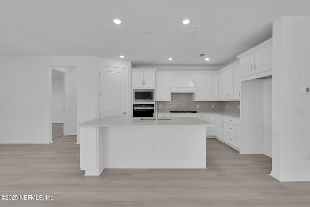 kitchen featuring premium range hood, light countertops, decorative backsplash, white cabinets, and black appliances