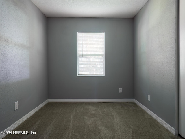 spare room featuring dark colored carpet and a textured ceiling