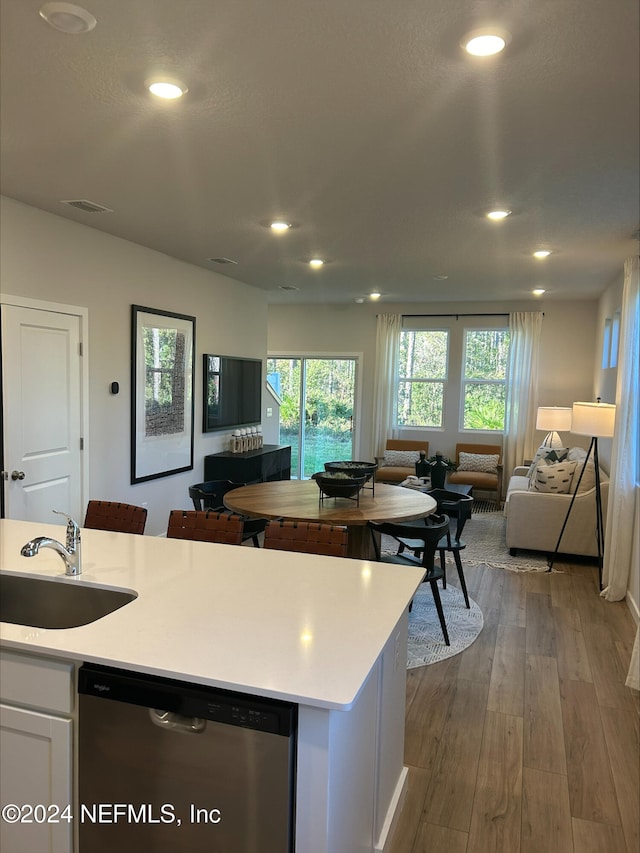 kitchen featuring stainless steel dishwasher, a kitchen island with sink, sink, hardwood / wood-style floors, and white cabinetry