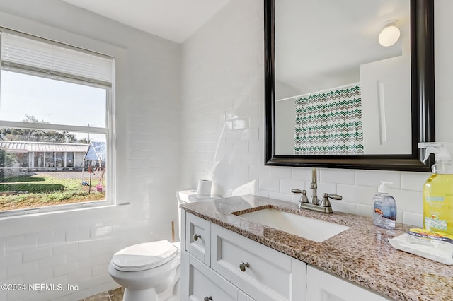 bathroom with walk in shower, backsplash, toilet, vanity, and tile walls