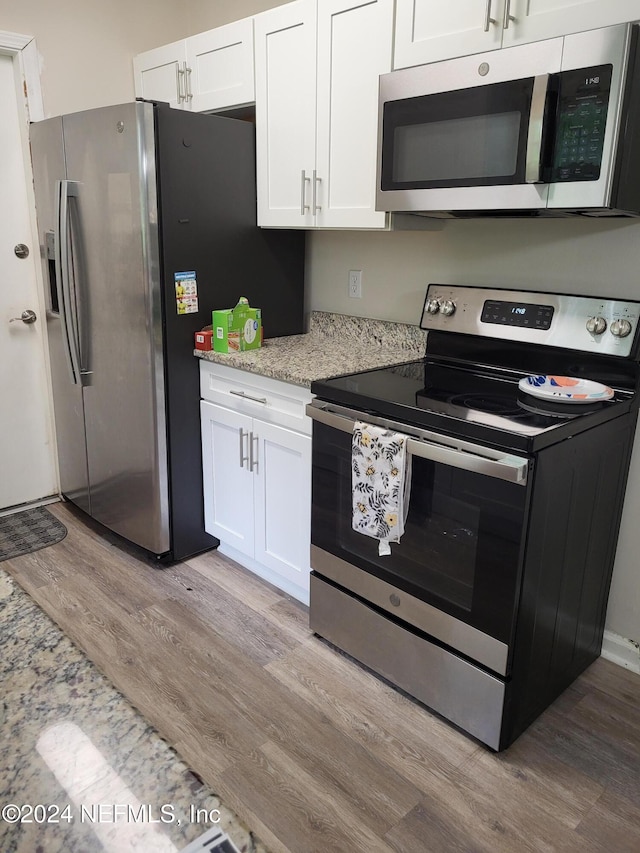 kitchen featuring white cabinets, appliances with stainless steel finishes, light hardwood / wood-style floors, and light stone countertops