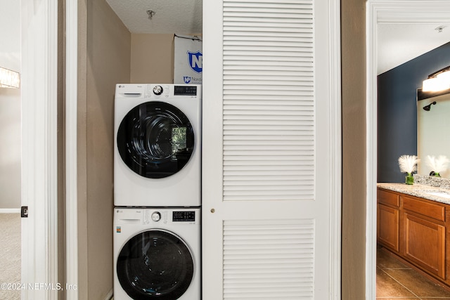 clothes washing area featuring stacked washer / dryer, light tile patterned floors, and a textured ceiling