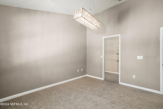 carpeted spare room with a textured ceiling and an inviting chandelier