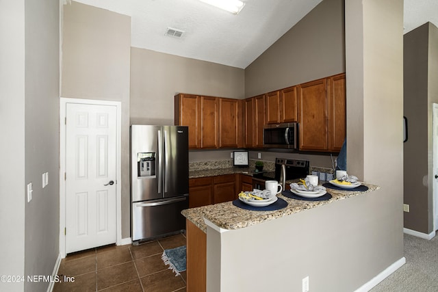 kitchen with dark tile patterned flooring, light stone counters, kitchen peninsula, and stainless steel appliances