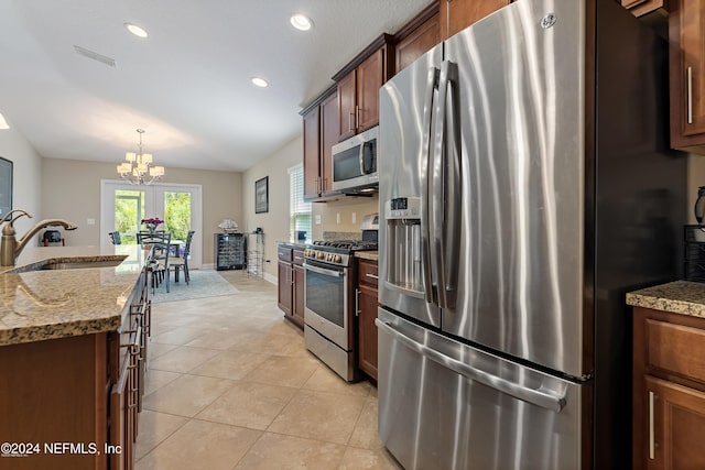 kitchen with appliances with stainless steel finishes, light stone counters, sink, a chandelier, and hanging light fixtures