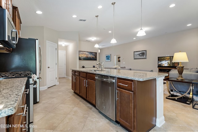 kitchen featuring sink, hanging light fixtures, light stone counters, an island with sink, and appliances with stainless steel finishes