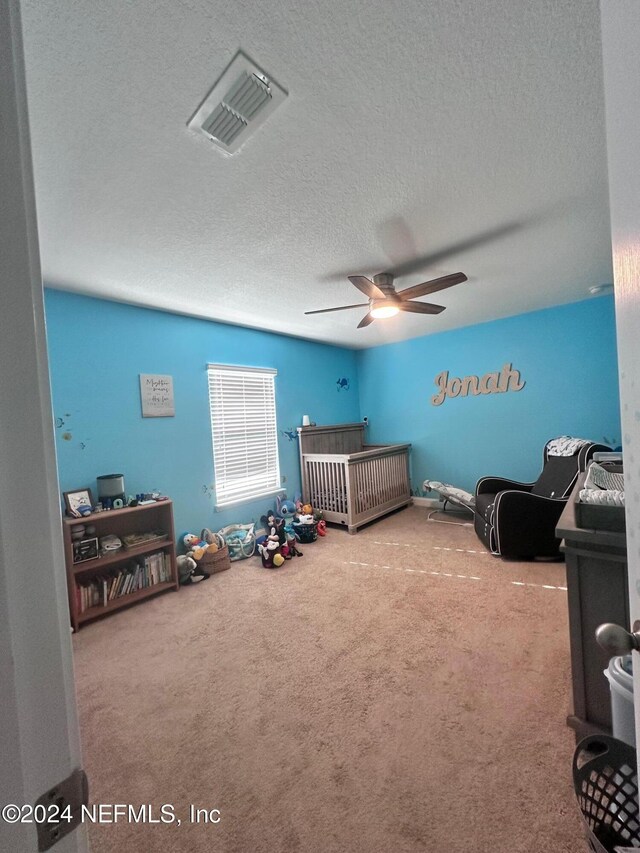 carpeted bedroom featuring ceiling fan, a textured ceiling, and a nursery area