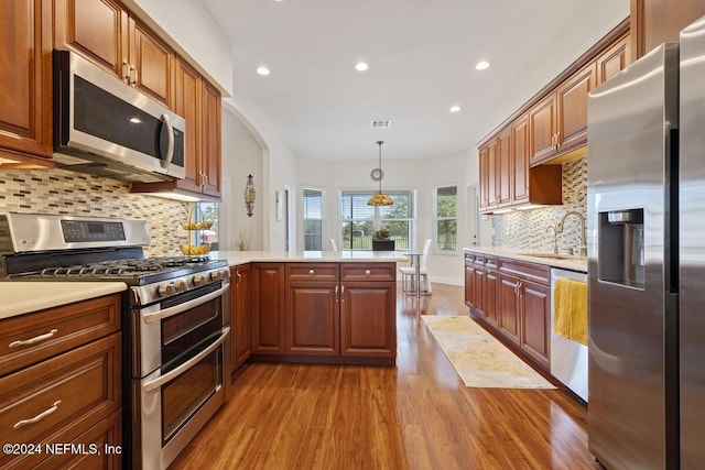 kitchen featuring sink, decorative light fixtures, light hardwood / wood-style floors, kitchen peninsula, and stainless steel appliances