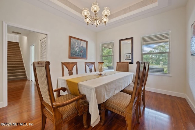 dining space with dark hardwood / wood-style flooring, a tray ceiling, and an inviting chandelier