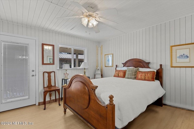 bedroom with access to outside, ceiling fan, light hardwood / wood-style flooring, and wooden walls