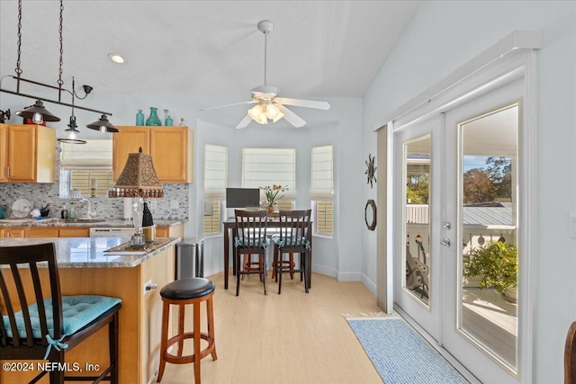 kitchen with ceiling fan, tasteful backsplash, light stone counters, light hardwood / wood-style floors, and a kitchen bar