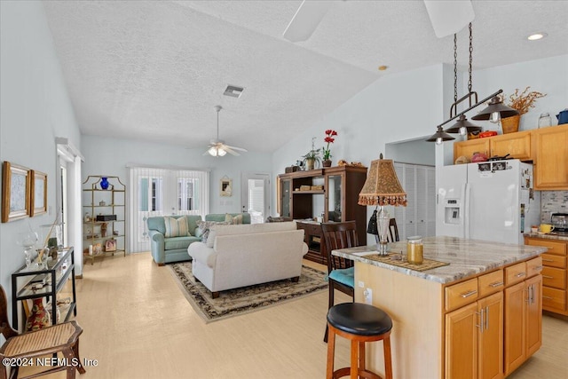 kitchen featuring vaulted ceiling, ceiling fan, white refrigerator with ice dispenser, light hardwood / wood-style floors, and a kitchen island