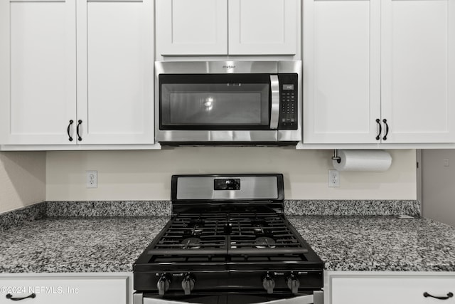 kitchen with gas stove, dark stone countertops, and white cabinetry