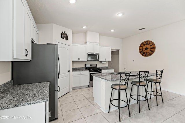 kitchen featuring a breakfast bar, stainless steel appliances, a center island with sink, stone countertops, and white cabinetry