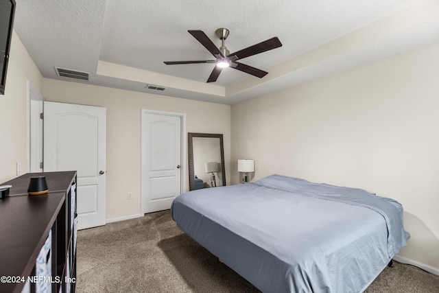 bedroom featuring ceiling fan, dark carpet, a raised ceiling, and a textured ceiling