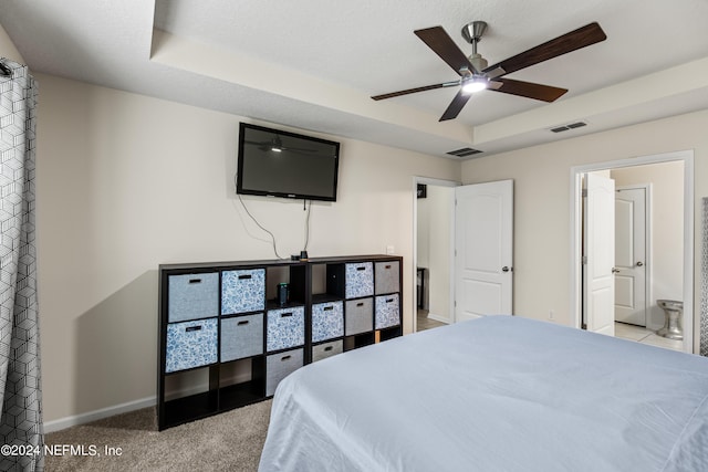 carpeted bedroom with a raised ceiling, ensuite bath, and ceiling fan