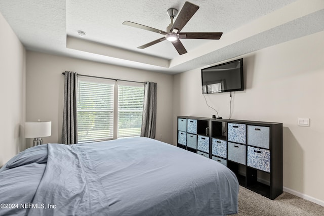 bedroom featuring carpet flooring, a textured ceiling, a tray ceiling, and ceiling fan