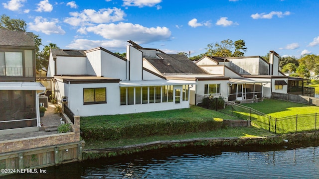 rear view of property with a sunroom, a yard, and a water view