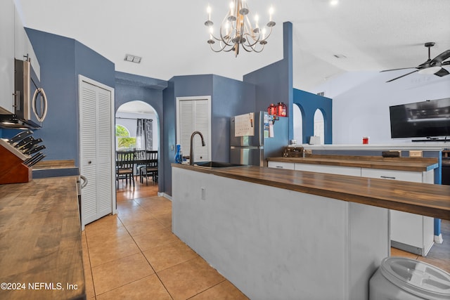 kitchen featuring butcher block countertops, pendant lighting, vaulted ceiling, light tile patterned floors, and appliances with stainless steel finishes