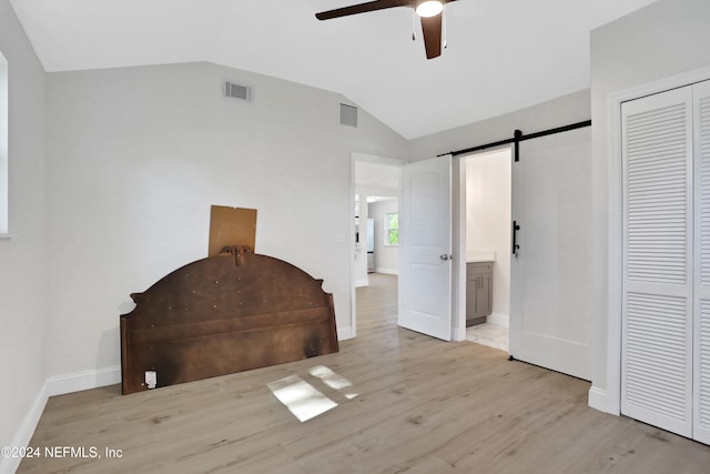 unfurnished bedroom with ceiling fan, a barn door, light hardwood / wood-style floors, a closet, and lofted ceiling