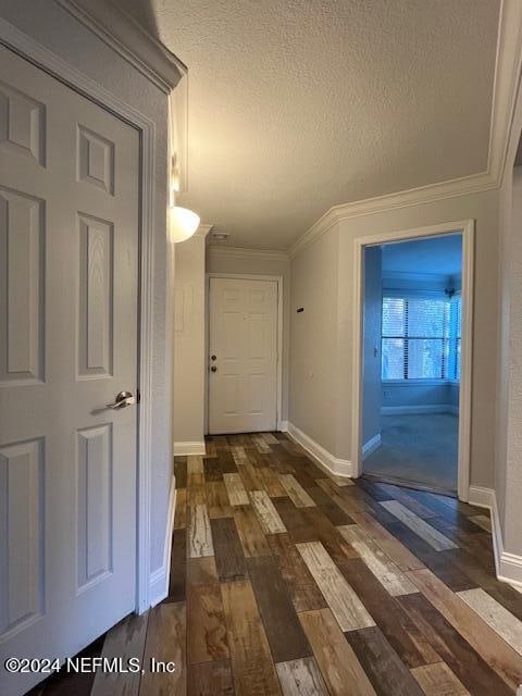 corridor with ornamental molding, a textured ceiling, and dark wood-type flooring