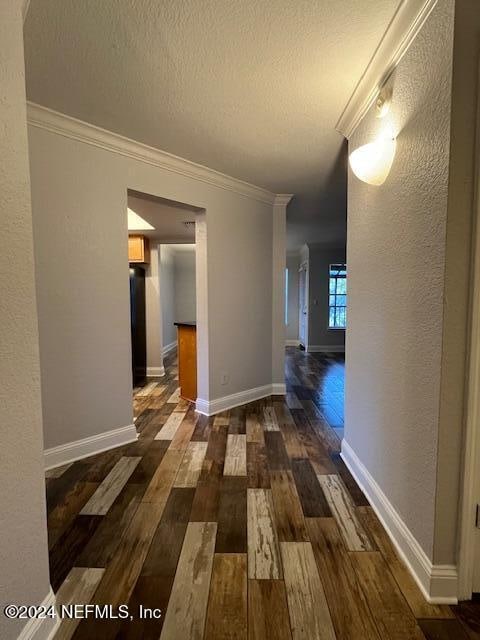 corridor with dark hardwood / wood-style flooring, ornamental molding, and a textured ceiling