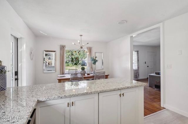 kitchen featuring white cabinetry, light stone countertops, hanging light fixtures, a chandelier, and light wood-type flooring