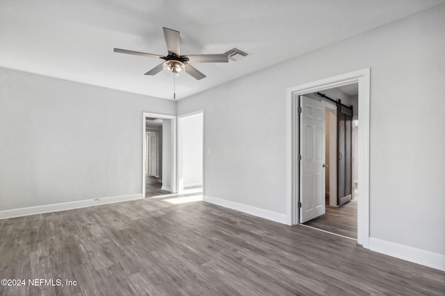 empty room with ceiling fan, a barn door, and dark hardwood / wood-style flooring