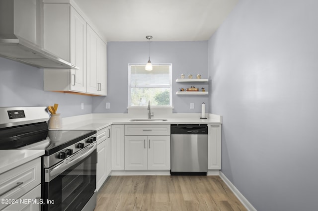 kitchen with stainless steel appliances, light countertops, wall chimney range hood, white cabinetry, and a sink