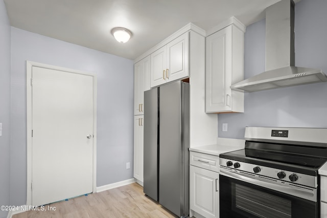 kitchen featuring light wood-style floors, stainless steel appliances, light countertops, wall chimney range hood, and white cabinetry