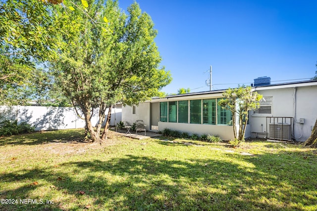 back of property with central AC, fence, and a lawn