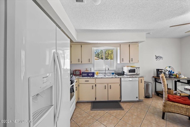 kitchen featuring cream cabinetry, white appliances, sink, and light tile patterned floors