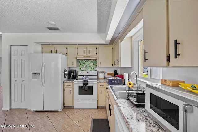 kitchen with a textured ceiling, sink, white appliances, and cream cabinetry